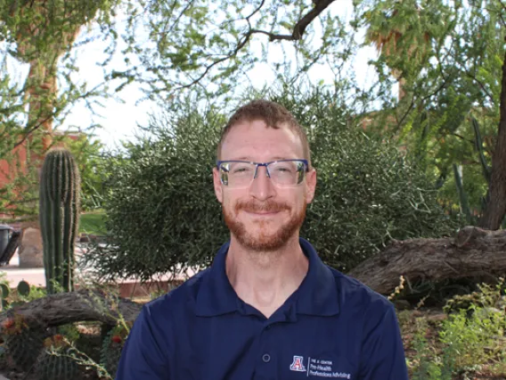 image of a man wearing glasses, posed in front of a curated desert landscape